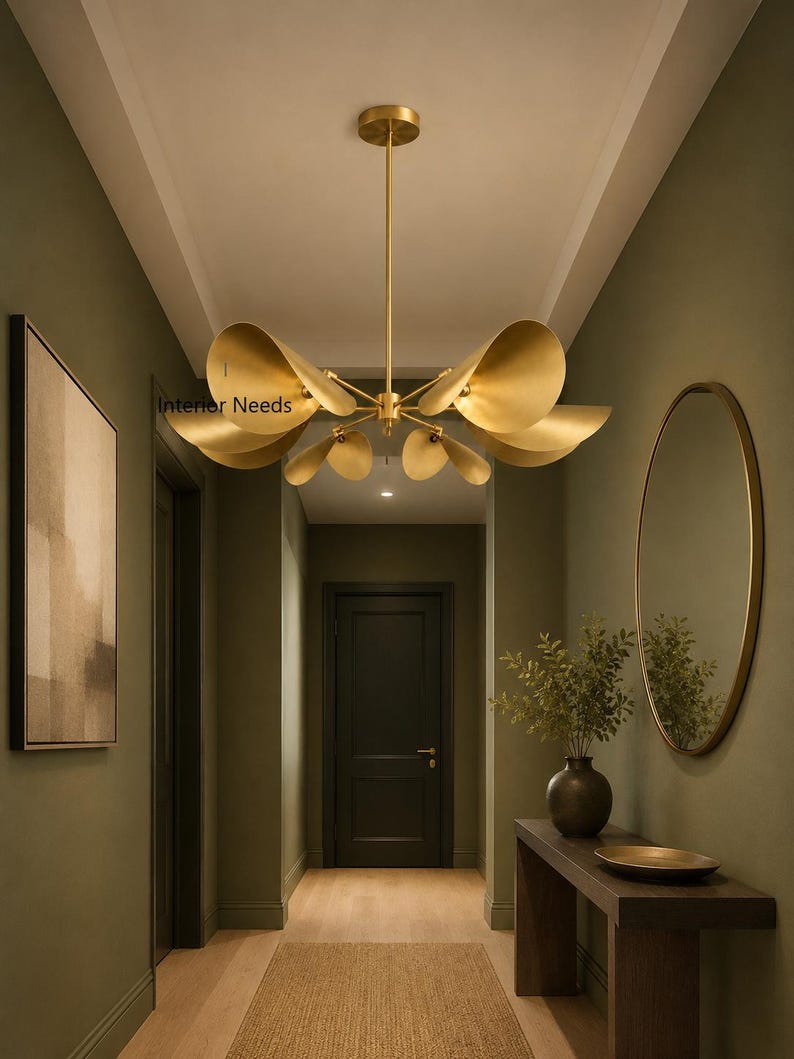 May include: A gold-toned metal chandelier featuring multiple trumpet-shaped shades arranged in a radial pattern, suspended from a central rod. The fixture includes the text Interior Needs printed on one of the metallic shades in black lettering.