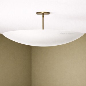 May include: A modern, white, oval-shaped ceiling light fixture with a brass-colored stem and ceiling mount. The fixture is suspended from the ceiling and provides ambient lighting. The text "Interior Needs" is visible on the light.