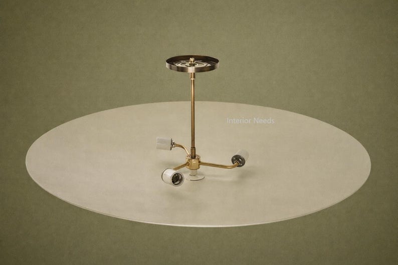 May include: A mid-century modern ceiling light fixture with a brass finish and three light sockets. The fixture is mounted on a large, round, off-white shade. The background is a muted olive green.