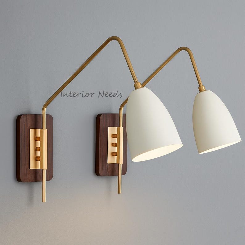 May include: Two wall sconces featuring white, cone-shaped shades and brass-toned arms. They are mounted on rectangular wooden backplates with brass detailing. The text "Interior Needs" is visible on the wall.