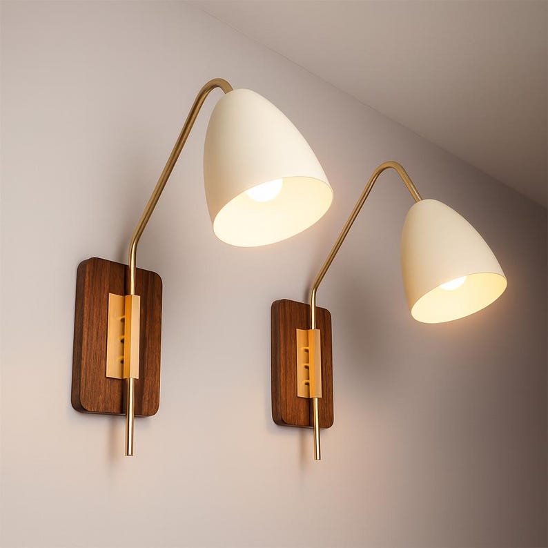 May include: Two mid-century modern wall sconces. Each sconce has a cream-coloured, cone-shaped shade, a brass-coloured curved arm, and a rectangular wooden base with a gold-coloured accent. The sconces are mounted on a light-coloured wall.