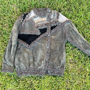 Puede incluir: Chaqueta vintage de ante en tonos verde oliva, marrón y negro, con un diseño de patchwork único. La chaqueta presenta un cuello alto, cierre de botones y ribete texturizado a lo largo de los bordes, creando una estética bohemia.