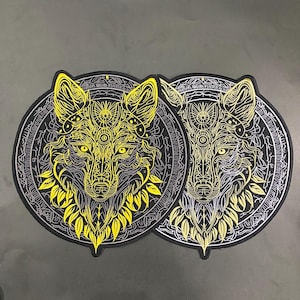 May include: Two circular patches featuring a detailed wolf head design. The wolf's face is rendered in yellow and silver against a black background, with intricate patterns and a decorative border. The patches are likely for clothing or accessories.
