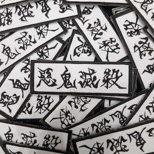 May include: A collection of white rectangular patches with black borders and Japanese calligraphy. The patches are densely arranged, with the black characters standing out against the white background. The image is a close-up shot.