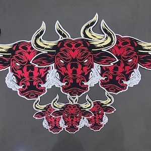 Op de afbeelding: Geborduurde patches met een gestileerde stierenkop met rode en zwarte details, gouden hoorns en witte rook. De patches zijn gegroepeerd op een grijze achtergrond. Het gezicht van de stier heeft een boze uitdrukking.