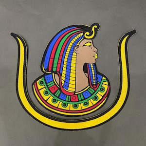 May include: Embroidered patch featuring a profile of an Egyptian figure with a colorful headdress. The patch has a brown face, gold accents, and a yellow border. The headdress includes blue, red, green, and yellow stripes. The patch is in the shape of a U.