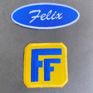 Könnte beinhalten: Zwei gestickte Aufnäher. Der obere Aufnäher ist oval mit blauem Hintergrund und dem Namen "Felix" in weißer Schrift. Der untere Aufnäher ist ein gelbes Quadrat mit blauem "FF"-Design.