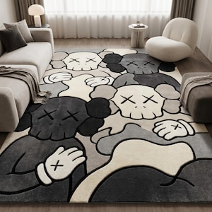 Striking modern rug in a minimalist living room. It features a dense wool texture and an abstract pattern of overlapping Kaws style companion figures with crossed eyes and gloved hands, rendered in rich shades of cream, light grey, dark grey, and black. The plush hand-carved design feels upscale and contemporary on a warm wood floor.