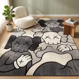 Striking modern rug in a minimalist living room. It features a dense wool texture and an abstract pattern of overlapping Kaws style companion figures with crossed eyes and gloved hands, rendered in rich shades of cream, light grey, dark grey, and black. The plush hand-carved design feels upscale and contemporary on a warm wood floor.