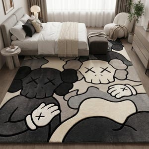 Striking modern rug in a minimalist living room. It features a dense wool texture and an abstract pattern of overlapping Kaws style companion figures with crossed eyes and gloved hands, rendered in rich shades of cream, light grey, dark grey, and black. The plush hand-carved design feels upscale and contemporary on a warm wood floor.