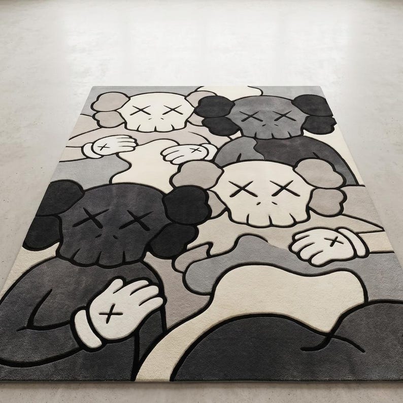Striking modern rug in a minimalist living room. It features a dense wool texture and an abstract pattern of overlapping Kaws style companion figures with crossed eyes and gloved hands, rendered in rich shades of cream, light grey, dark grey, and black. The plush hand-carved design feels upscale and contemporary on a warm wood floor.