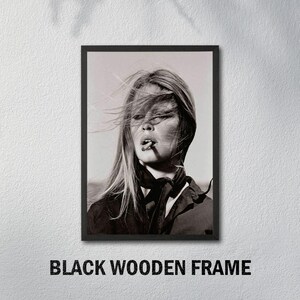 May include: Black and white framed print featuring a portrait of a woman with long hair, smoking a cigarette. The image is set against a neutral background and framed in a black wooden frame. The text "BLACK WOODEN FRAME" is at the bottom.