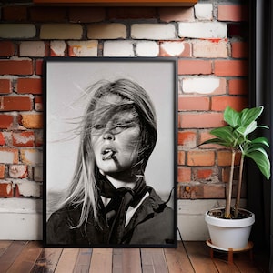 May include: Black and white framed portrait of a woman with long hair, smoking a cigarette. The image is a close-up, with the woman's face and upper body visible. She is wearing a dark top and a scarf.