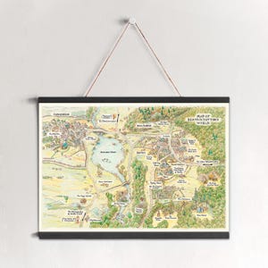 Könnte beinhalten: Eine gerahmte Karte von Beatrix Potters Welt, die eine detaillierte, illustrierte Landschaft mit Städten, Gewässern und grünem Laub zeigt. Die Karte wird von einem schwarzen Magnetrahmen gehalten und an einer braunen Schnur aufgehängt.