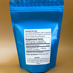 K&ouml;nnte beinhalten: Ein blauer Beutel mit Ashwagandha-Wurzelkapseln. Das Etikett enth&auml;lt N&auml;hrwertangaben, Anwendungshinweise und einen Warnhinweis. Die Portionsgr&ouml;&szlig;e betr&auml;gt 2 Kapseln, mit 90 Portionen pro Beh&auml;lter. Jede Portion enth&auml;lt 1.000 mg Ashwagandha-Wurzel.