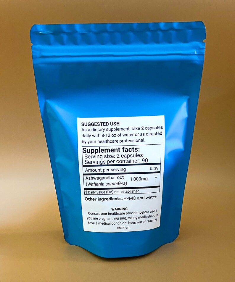 K&ouml;nnte beinhalten: Ein blauer Beutel mit Ashwagandha-Wurzelkapseln. Das Etikett enth&auml;lt N&auml;hrwertangaben, Anwendungshinweise und einen Warnhinweis. Die Portionsgr&ouml;&szlig;e betr&auml;gt 2 Kapseln, mit 90 Portionen pro Beh&auml;lter. Jede Portion enth&auml;lt 1.000 mg Ashwagandha-Wurzel.
