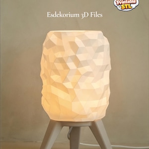 May include: A white geometric-patterned lamp with a warm glow, resting on a three-legged stand. The lamp's shade features a textured, faceted design. The text "Esdekorium 3D Files" is visible.