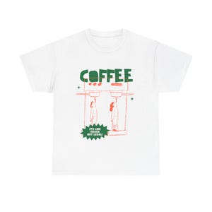 May include: White t-shirt featuring a green and red graphic. The word "COFFEE" is printed in green above a red illustration of two figures. Below the illustration is the text "IT'S LIKE CRACK BUT LEGAL!" in a green starburst.