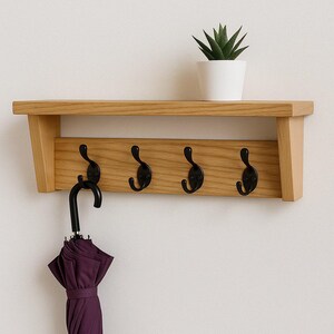 May include: Wooden wall-mounted shelf with four black hooks and a small white potted plant. A closed purple umbrella hangs from one hook. The shelf is made of light-colored wood.
