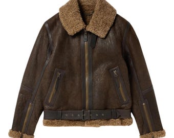 May include: A brown leather jacket with a shearling collar and lining. The jacket features a zip-up front, multiple zippered pockets, and a buckled belt at the waist. The jacket has a classic aviator style.