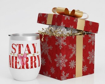 以下が含まれることがあります： 「STAY MERRY」の文字が赤いグリッターで書かれ、ピンクのリボンと星のアクセントが付いた白い断熱ワインタンブラー。その隣には、金色のリボンと雪の結晶模様の赤いギフトボックスがあります。