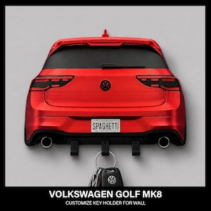 May include: A red wall-mounted key holder shaped like the rear of a Volkswagen Golf MK8. It features black taillights, a black logo, and a licence plate that reads Ontario SPAGHETTI. Three black hooks extend from the bottom, holding a metal keyring.