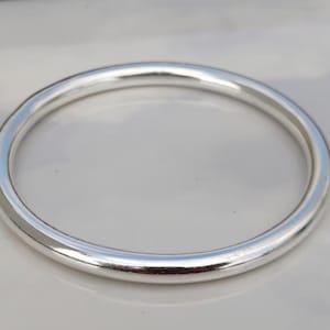 May include: A solid, silver-colored bangle bracelet. The bracelet is a simple, circular design with a smooth, polished surface. The bangle is approximately 2.5 inches in diameter.