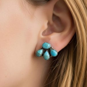 May include: A silver-toned stud earring featuring five turquoise-colored stones. The stones are arranged in a cluster, with a mix of oval and teardrop shapes. The earring is worn on an ear.