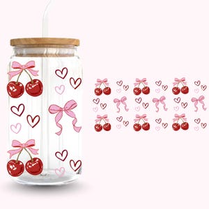 Pu&ograve; includere: Un bicchiere di vetro trasparente con coperchio in legno e cannuccia. Il bicchiere &egrave; decorato con ciliegie rosse legate con fiocchi rosa e cuori rosa e rosa scuro. Lo sfondo &egrave; rosa chiaro.