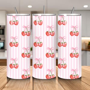 May include: Three stainless steel tumblers with a pink and white striped pattern. Each tumbler features a repeating watercolor design of strawberries tied with pink bows. The tumblers have a silver straw.