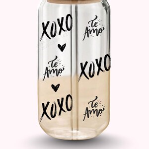 Pu&ograve; includere: Un contenitore per bevande in vetro trasparente con coperchio in legno. Il contenitore &egrave; decorato con le parole "XOXO" e "Te Amo" in grafia nera, insieme a simboli di cuore neri. La met&agrave; inferiore del contenitore ha una tonalit&agrave; marrone chiaro.