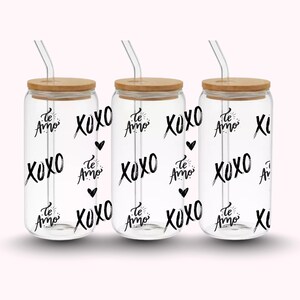Pu&ograve; includere: Tre bicchieri di vetro trasparente con coperchi in bamb&ugrave; e cannucce di vetro. I bicchieri sono decorati con le parole "Te Amo" e "XOXO" in grafia nera, insieme a piccole grafiche a cuore nere. I bicchieri sono su uno sfondo rosa chiaro.