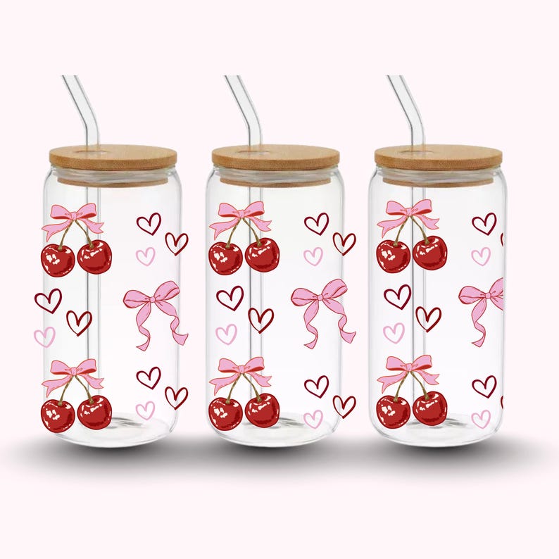Pu&ograve; includere: Tre bicchieri di vetro trasparente con coperchi in bamb&ugrave; e cannucce di vetro. Ogni bicchiere presenta un design a ciliegia con fiocchi rosa e cuori. Le ciliegie sono rosse e i fiocchi sono rosa.