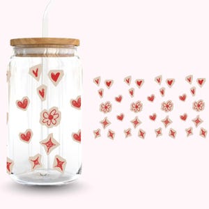 Pu&ograve; includere: Un barattolo di vetro trasparente con coperchio in legno e cannuccia. Il barattolo &egrave; decorato con disegni rossi a forma di cuore, fiore e stella su carta strappata. Lo sfondo &egrave; rosa tenue.