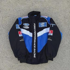 Op de afbeelding: Zwarte, blauwe en witte Ford Performance Racing jas. De jas heeft meerdere sponsorlogo's, een blauw-wit chevronontwerp op de voorkant en de tekst "FORD PERFORMANCE RACING" verticaal.