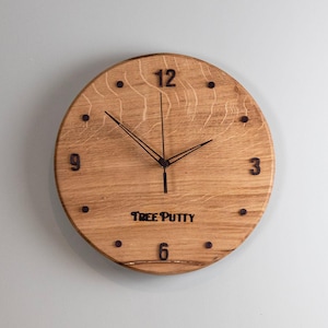 May include: A circular wooden clock with black numerals and hands. The clock face is light brown with wood grain. The text "TREE PUTTY" is printed below the centre.