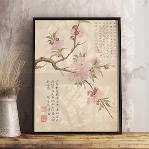 May include: A framed print featuring a watercolor painting of pink blossoms on a branch, with green leaves. The artwork has Chinese characters and red stamps. The print is displayed on a wooden surface.