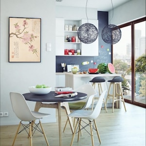 May include: A modern dining room with a round black table and four white chairs with wooden legs. Two spherical pendant lights hang above a kitchen island with bar stools. A framed floral print hangs on the wall.