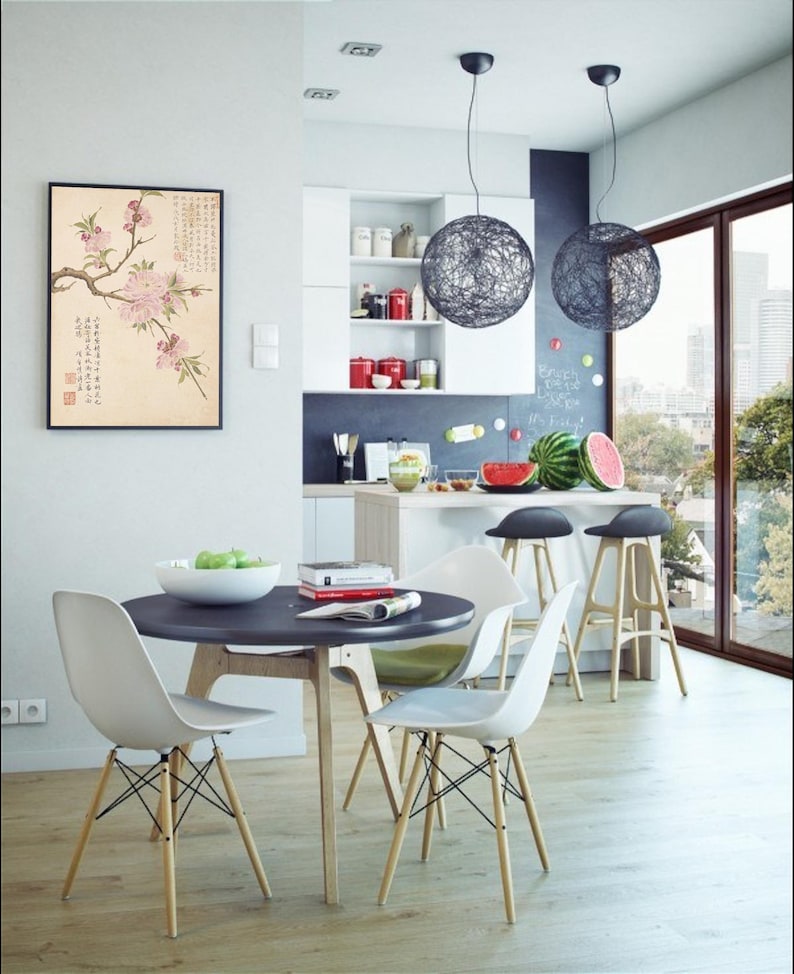 May include: A modern dining room with a round black table and four white chairs with wooden legs. Two spherical pendant lights hang above a kitchen island with bar stools. A framed floral print hangs on the wall.