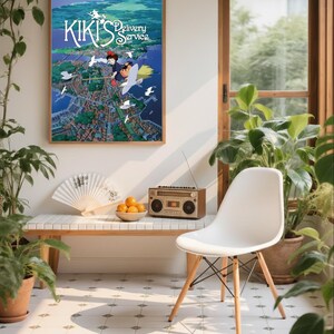 K&ouml;nnte beinhalten: Ein gerahmtes Poster von "Kikis kleiner Lieferservice" h&auml;ngt &uuml;ber einer Bank mit einem F&auml;cher und einer Schale mit Orangen. Ein Vintage-Radio steht auf der Bank. Ein wei&szlig;er Stuhl mit Holzbeinen steht neben der Bank. Topfpflanzen umgeben die Szene.