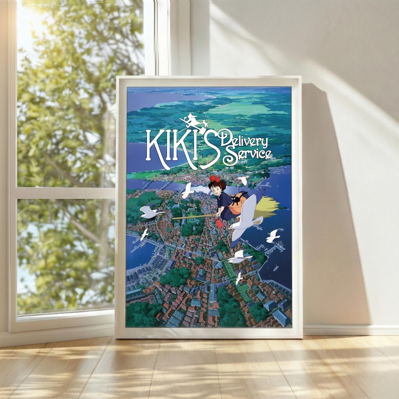K&ouml;nnte beinhalten: Gerahmtes Poster mit dem animierten Film "Kikis kleiner Lieferservice". Das Kunstwerk zeigt eine junge Hexe, die &uuml;ber einer K&uuml;stenstadt fliegt, mit dem Titel des Films prominent dargestellt. Die Farbpalette umfasst Blau-, Gr&uuml;n- und Wei&szlig;t&ouml;ne.