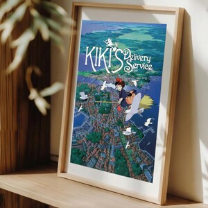 K&ouml;nnte beinhalten: Ein gerahmter Druck des Animationsfilms "Kikis kleiner Lieferservice". Das Kunstwerk zeigt eine junge Hexe auf einem Besen &uuml;ber einer K&uuml;stenstadt, mit dem Titeltext in einer stilisierten Schriftart. Die Farbpalette umfasst Blau-, Gr&uuml;n- und Wei&szlig;t&ouml;ne.