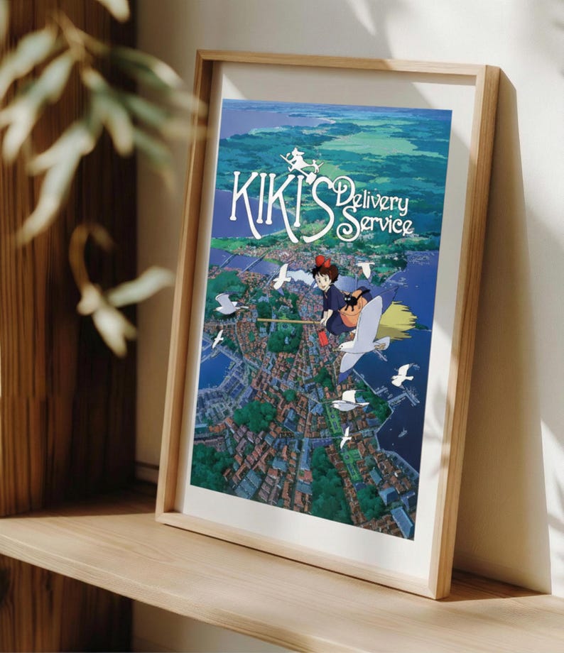 K&ouml;nnte beinhalten: Ein gerahmter Druck des Animationsfilms "Kikis kleiner Lieferservice". Das Kunstwerk zeigt eine junge Hexe auf einem Besen &uuml;ber einer K&uuml;stenstadt, mit dem Titeltext in einer stilisierten Schriftart. Die Farbpalette umfasst Blau-, Gr&uuml;n- und Wei&szlig;t&ouml;ne.