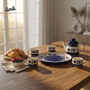 Peut inclure: Un service à thé en céramique orné d'un motif floral bleu foncé et crème, comprenant une théière, trois tasses et un grand plateau rond. Un petit bol rempli de baies fraîches est posé à côté d'une planche en bois avec trois croissants.