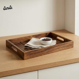 Puede incluir: Una taza de cerámica blanca con un asa negra y el texto "But First, Coffee" en negrita negra. La taza se encuentra sobre un fondo borroso, sugiriendo un ambiente acogedor.