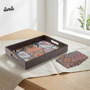 Puede incluir: Una bandeja rectangular marrón con asas recortadas, con un colorido diseño de patchwork de patrones geométricos y florales. Posavasos con diseños a juego están junto a la bandeja. La bandeja y los posavasos están sobre un mantel de color claro.