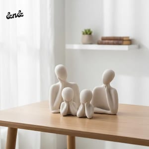Puede incluir: Una escultura familiar minimalista en una paleta de colores neutros. Las figuras abstractas, dos adultos y dos niños, están dispuestas sobre una mesa de madera. Un elemento decorativo para un espacio vital moderno.