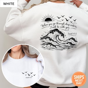 May include: A white sweatshirt featuring a black graphic print. The back displays a large ocean wave, a rising sun, birds, and the text "When you go through deep waters, I will be with you. Isaiah 43:2". The front chest area shows small birds and "Isaiah 43:2".