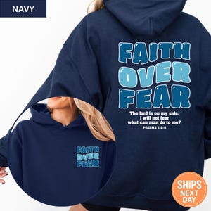 May include: Navy blue hoodie with the text "FAITH OVER FEAR" in a light blue bubble font on the back. The front of the hoodie has the same text in a smaller size. The text "The lord is on my side: I will not fear what can man do to me? Psalms 118:0" is also on the back.