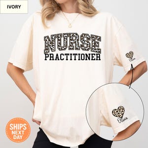 May include: Ivory-colored t-shirt with the words "NURSE PRACTITIONER" in black block letters with a leopard print fill. A leopard print heart with the name "Olivia" is on the sleeve. The shirt has short sleeves.